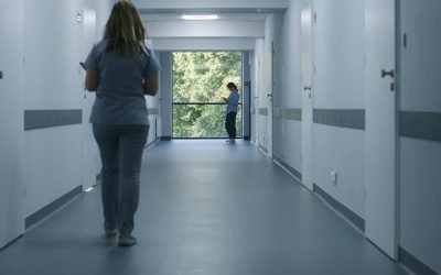 Clinic corridor: Doctors and professional medics walk. Nurse with digital tablet comes to female patient standing near window. Medical staff and patients in modern hospital or medical center hallway.