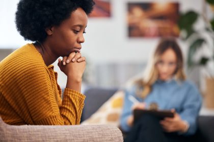 A women sites with her hands resting under her chin while a counselor takes notes