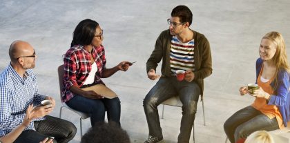 A man sits in a group setting, talking to another group member and holding a coffee cup